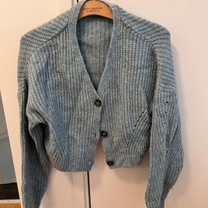 Ljusblå stickad kofta från NA-KD - Supermysig ljusblå stickad kofta från NA-KD med chunky struktur och stora knappar framtill. Koftan har v-ringning, lång ärm och ribbade muddar.