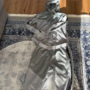 Grå Nike hoodie med dragkedja - Snygg grå Nike hoodie med hel dragkedja och huva. Tröjan har svarta detaljer med vita Nike-loggor längs ärmarna och snörning i huvan. Perfekt för dig som gillar sportig och stilren look.