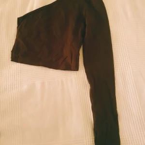 Svart oneshoulder topp - Säljer en svart oneshoulder topp med lång ärm. Toppen är croppad och har en stilren, minimalistisk look som passar perfekt till jeans eller kjol. Gjord i mjukt material som sitter skönt mot kroppen.  Storleks lappen saknas, lite ljusare i färgen & tvättludd