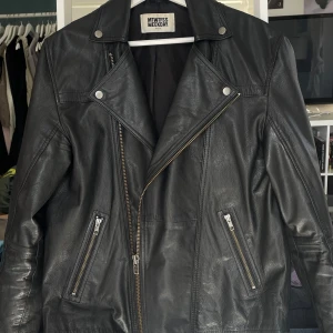 Svart skinnjacka från Weekday - Säljer en svart skinnjacka från Weekday i klassisk bikerstil. Jackan har sned dragkedja, breda slag med tryckknappar och två fickor med dragkedja framtill. Snygg passform och perfekt för dig som vill ha en edgy look. Mycket rejäl kvalitet. I killstorlek, men passar bra upp till en L i tjejstorlek. Endast använd ett par gånger. 