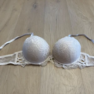 Vit spets bandeau från Censored - Snygg vit bandeau från Censored med vacker spets och blommigt mönster. Axelbandslös design med vadderade kupor och fina snörningsdetaljer i sidorna. Perfekt för dig som vill ha en feminin och stilren look.