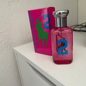 Ralph Lauren Big Pony 2 Parfym 50ml NY/OANVÄND köptes för 680kr på kicks - Rosa parfymflaska från Ralph Lauren Big Pony Collection, nummer 2, för kvinnor. Flaskan är i glas med blått tryck och silverfärgad kork. Kartongen är starkt rosa med grönt och blått tryck, och parfymen har en fruktig och sensuell doft. FELKÖP DÄRAV PRISET KÖPTE DEN FÖR 680kr på kicks