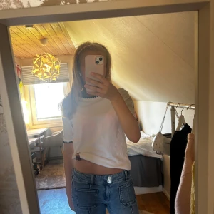 Vit t-shirt med svarta detaljer - Vit t-shirt med korta ärmar och svarta vågiga detaljer vid ärmslut och halsringning. Modellen är rak och lite loose fit, perfekt till jeans eller kjol. Enkel och stilren design utan tryck eller mönster.