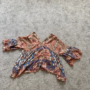 Mönstrad blus från Zara  - Supersnygg blus från Zara med mönster i brunt, blått och beige. Blusen har v-ringning, knappar framtill och vida trekvartsärmar. Perfekt för dig som gillar unika detaljer och färgstarka plagg.