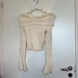 Offshoulder stickad tröja i beige -  Offshoulder stickad tröja i beige med ribbad struktur och långa ärmar. Tröjan har en bred krage som vilar över axlarna och en snygg halterneck-detalj. Köpt från ett okänt märke på Yesstyle. Helt oanvänd, endast provad.