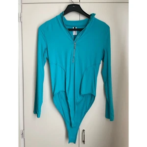 🌊 Helt ny turkos långärmad bodysuit/baddräkt från MOTF – Strl L 🌊 - Säljer en helt ny och oanvänd långärmad bodysuit/baddräkt i en härlig turkos färg från MOTF (Shein) – lapparna sitter fortfarande kvar! Plagget är i storlek L och har ett sportigt, stilrent snitt med hög krage och praktisk dragkedja framtill.  Supermångsidig – använd den som: ✔️ Rashguard/UV-tröja vid stranden eller vid vattensport (t.ex. SUP, surfing) ✔️ Träningsbody för dans, yoga eller gym ✔️ Snygg body att matcha med jeans, kjol eller shorts för en trendig streetwear-look 🩵 