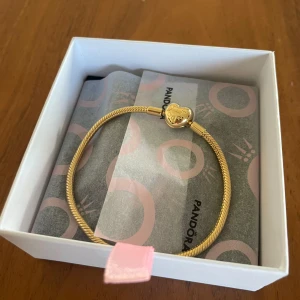 Guldarmband med hjärtlås från Pandora - Snyggt guldarmband från Pandora med ett hjärtformat lås där Pandora-loggan är ingraverad. Helt nytt, då de inte passa. Självklart äkta!❣️