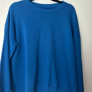 Blå sweatshirt från 157 - Enkel och stilren blå sweatshirt från 157 i storlek XS/S. Tröjan har rund halsringning, långa ärmar och ribbade muddar vid hals, ärmslut och nederkant. Perfekt för en chill och avslappnad look.