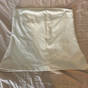Vit satinliknande tub topp L Kappahl  - Supersnygg vit topp i satinliknande material med lätt glans. Kjolen har en enkel och stilren design med lätt A-linjeformad passform. Perfekt att styla med en crop top eller oversized skjorta för en trendig look.