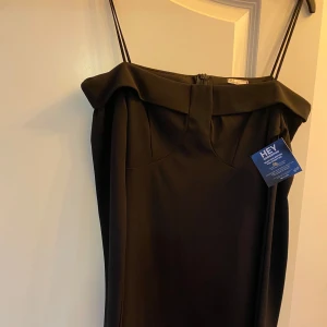 Svart axelbandslös kortklänning H&M - Stilren svart kortklänning från H&M med avtagbara tunna axelband och bred offshoulder-krage. Klänningen har en figurnära passform och dragkedja bak. Perfekt för dig som gillar minimalistisk och elegant stil. Helt oanvänd och prispappen finns kvar.