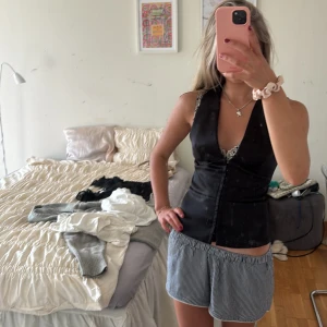 Svart satinväst från Zara - Säljer en svart väst från Zara i glansigt satinmaterial. Västen har djup v-ringning, figurnära passform och knäppning framtill med små knappar. Perfekt att styla över en topp eller skjorta för en trendig look.. pris kan diskuteras 