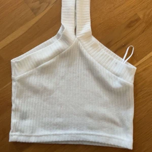 Vit ribbad croppad linnetopp - Säljer en vit ribbad linnetopp med breda axelband som delar sig framtill. Toppen är croppad och har en snygg, enkel design som passar perfekt till jeans eller kjol. Materialet är mjukt och stretchigt för en bekväm känsla. Tyvärr några fläckar på banden, går möjligtvis bort i tvätten och med något borttagningsmedel🤍