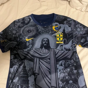  Brazil fotbollströja - Snygg marinblå Brasilien fotbollströja från Nike med unikt grafiskt tryck av Kristusstatyn och brasilianska symboler. Oänvänd