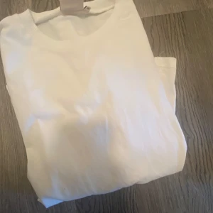 Vit omlottopp med knyt från Nelly - Säljer en stilren vit omlottopp från Nelly i storlek XS. Toppen har långa ärmar och knyt framtill som ger en snygg och trendig look. Perfekt att matcha med jeans eller kjol för en fräsch outfit.