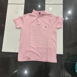 Ljusrosa pikétröja från Polo Ralph Lauren - Säljer en ljusrosa pikétröja från Polo Ralph Lauren i bomull. Klassisk krage, korta ärmar och liten broderad logga på bröstet. Perfekt för dig som gillar stilren och avslappnad look.