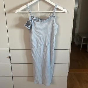Ljusblå klänning från Pieces - Supersöt ljusblå kortklänning från Pieces i ribbad bomull med tunna axelband och volangdetaljer vid halsringningen. Klänningen har ett smalt, randigt mönster och är perfekt för varma dagar. Enkel och fräsch stil som känns både trendig och chill.