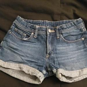 Jeansshorts från H&M, storlek 140 - Snygga jeansshorts från H&M i klassisk blå denim. De har en normal passform med upprullade benslut och femficksdesign. Perfekta för en avslappnad stil under varma dagar.