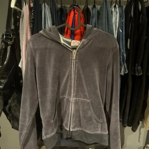 Grå velourjacka från Juicy Couture - Säljer en grå velourjacka från Juicy Couture med dragkedja och huva. I bra skick, några stenar har lossnat på baksidan. Står storlek L men passar S-M