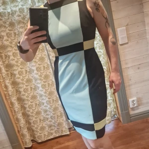 Retro klänning från Maggy London - Snygg retro klänning från Maggy London i en cool flerfärgad 60tals inspirerad design med svart, ljusblå och gul. Klänningen har en tight passform och är ärmlös, väldigt bekväm! Tyvärr har den luten fläck. Storlek xs men hade ber sagt s-m