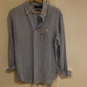 POLO RALPH LAUREN SKJORTA - Vit-blå randig linneskjorta fråga Ralph Lauren, storlek S, passar M. Skicket är 10/10, lappen sitter kvar!                                                                              Perfekt och ha till våren!