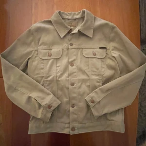 Nudie Jeans Jacka - Säljer en mycket snygg och stilren Nudie Jeans Co jacka (Robby 70s Sand) i ny skick. Jackan är använd typ 2 gånger och utan några skador. Skick: 10/10. Nypriset ligger på omkring 3000kr! Hör av dig vid eventuella frågor! 