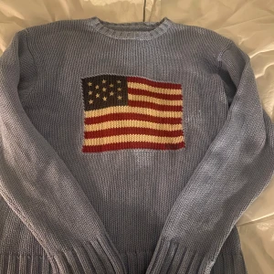 Blå stickad tröja med amerikansk flagga - Säljer en blå stickad tröja från Ralph Lauren med en stor amerikansk flagga på framsidan. Tröjan har långa ärmar och ribbade muddar vid ärmslut och nederkant, tror att det är storlek S men finns ingen lapp💗 vet ej om den är äkta men är en gammal design så tror det
