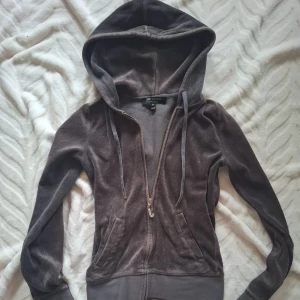 Brun/grå zip up från Juicy Couture💕 - Säljer en brun/grå zip up med guldiga detaljer från Juicy Couture i en mjuk bomullsblandning, dock känns materialet lite handuks likt men jätte fin ändå! 💘. Den har en dragkedja framtill och en dekorativ hängare med ett glittrigt 'J'. Tröjan är lite nopprig på insidan men verkligen inte något man tänker på! 💕 Det glittriga J:ett har dock förlorat några "diamanter" men de tänker man inte heller på! Säljer då den blivit för liten 😇 köpt här på plick! 