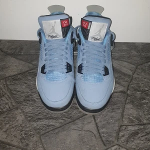 Nike Air Jordans i ljusblå mocka - Snygga Nike Air Jordans i ljusblå mocka med svarta och grå detaljer. Skorna har en klassisk snörning och en ikonisk Jumpman-logga på hälen. Perfekta för den som vill ha en stilren och sportig look.