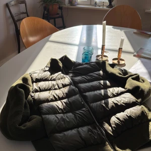 Bvaldi Olivgrön Cardigan - Säljer en olivgrön pufferjacka från Bvaldi med dragkedja och stickade detaljer. Jackan har en quiltad design och en praktisk ficka med knapp på ärmen. Perfekt för kyligare dagar. Perfekt passform och kvalité. Hör av er om ni vill ha fler bilder eller liknande.