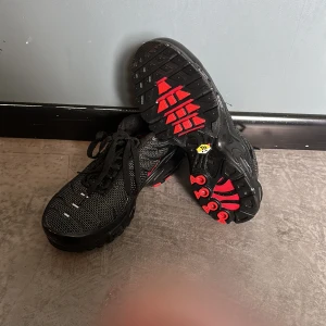Svarta och röda sneakers från Nike - Snygga svarta sneakers med röda detaljer från Nike. Skorna har en robust sula med bra grepp och klassisk snörning. Perfekta för en sportig look.