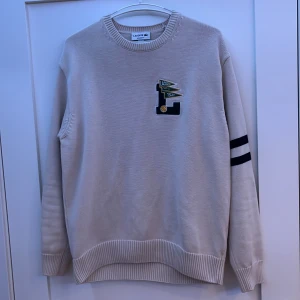 Stickad Lacoste tröja - En grädd vit stickad Lacoste tröja. Mycket bra skick. Fler bilder kan skickas om så önskas. (det var dåligt ljus på bilderna) 