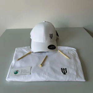 Vit keps med golfshopen logotyp - Snygg vit keps med en stilren broderad logotyp framtill. Kepsen har en klassisk design med justerbar passform och ventilationshål för extra komfort. Perfekt för en sportig look eller en avslappnad dag ute.
