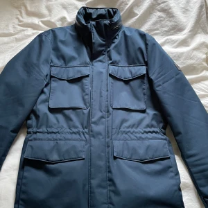 J Lindeberg jacka  - Mörkblå field jacka från J Lindeberg. Använd men fortfarande i väldigt bra skick. Modellen heter Tracher tech field jacket, nypris 2999 kr. Strl M men passar även L. Hör av er vid frågor!