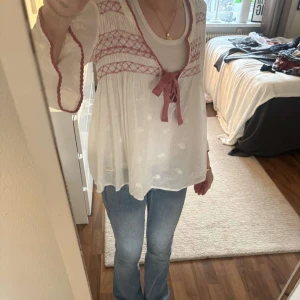 Sommar blus - En vit blus med rosa broderi mönster fram och baksida korta ärmar. En roset i mitt