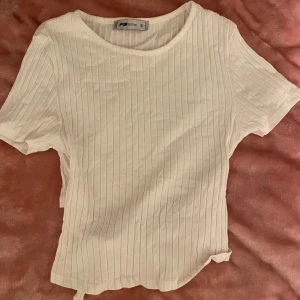 Vit ribbad topp från new yorker - Säljer en stilren vit ribbad topp från new yorker i storlek S. Toppen har korta ärmar och en knytning i ryggen som ger en snygg detalj. Perfekt för en avslappnad look.