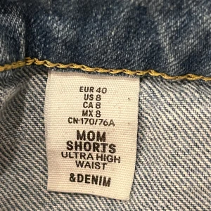 Blå mom shorts från &Denim - Säljer ett par blå mom shorts från &Denim med ultra hög midja. Shortsen har en sliten look med fransiga kanter och revor på framsidan. Perfekta för en avslappnad stil.