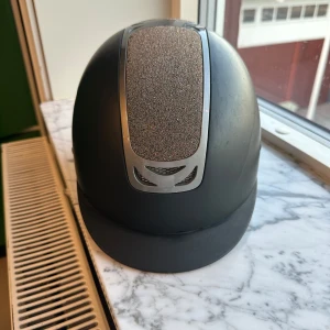 Ridhjälm från mips - Snygg svart ridhjälm med glittrig detalj på ovansidan. Hjälmen har en modern design med ventilationsöppningar och en justerbar rem för perfekt passform. Perfekt för den stilmedvetna ryttaren.