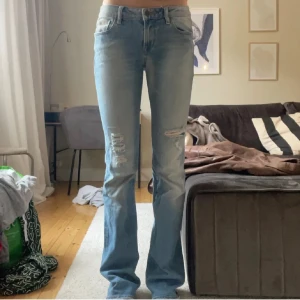 Blå bootcut jeans med slitningar - Snygga lågmidjade bootcut jeans med slitningar på låren. Storlek 27 men skulle säga att de lutar åt 28! Har ett litet större hål vid knät än på första bilderna😊Har även lagat jeansen pågrund av att de gått sönder(se bild 4 & 5) Men det är inget som syns på utsidan🥰 