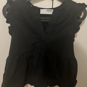 Svart blus från Selected Femme - Snygg svart blus från Selected Femme med volangdetaljer vid ärmarna och en v-ringad design. Perfekt för en stilren look.