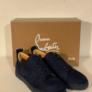 Mörkblå sneakers från Christian Louboutin - Snygga mörkblå sneakers från Christian Louboutin i mocka med den ikoniska röda sulan. Skorna har snörning och en stilren design som passar perfekt för en trendig look. Levereras med originalförpackning och dustbag.