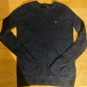 Stickad Morris tröja - Säljer en marinblå kabelstickad tröja med ett rött broderad Morris märke på bröstet. Tröjan är i jättebra skick.