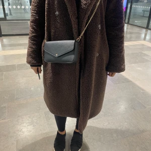 Brun teddyjacka - Mysig brun teddyjacka med knappar framtill. Perfekt för kyliga dagar med sin långa design och fluffiga material. Jackan har långa ärmar och en klassisk krage. Från bikbok i xs.