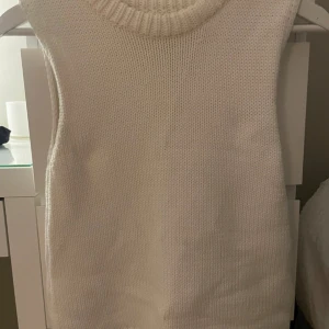 Vit stickad väst från Zara - Säljer en stilren vit stickad väst från Zara. Den har en ribbad rund halsringning och är perfekt för lager-på-lager-stil. Passar bra till både vardag och mer uppklädda tillfällen. Aldrig använd 