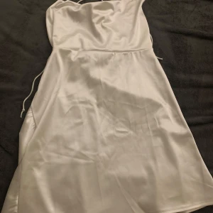 Vit axelbandslös klänning från Shein - Säljer en elegant vit axelbandslös klänning från Shein. Klänningen har en slät yta och smala axelband som korsar i ryggen för en stilren look. Perfekt för speciella tillfällen. 💫