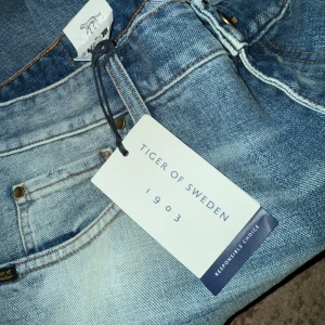 Blå jeans från Tiger of Sweden - Snygga blå jeans från Tiger of Sweden med en klassisk straight fit. De har en ljus tvätt och är tillverkade i ett slitstarkt denimtyg. Perfekta för en stilren look. Strl 36/32. Helt oanvända!