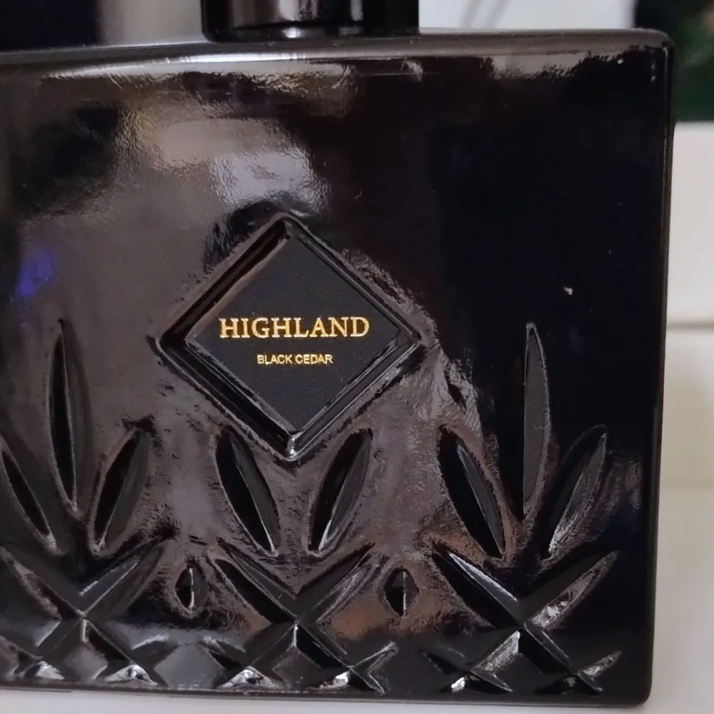 Elegant diffuser från Highland med doften Black Cedar. Flaskan är svart med ett stilrent mönster och guldtext. Perfekt för att skapa en lyxig atmosfär i hemmet.. Muu.