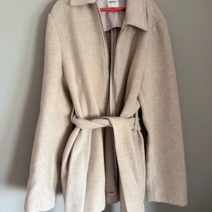 Beige kappa från Dobber - Snygg beige kappa från Dobber med dragkedja och bälte i midjan. Perfekt för höst och vår. Tyvärr knappt använd pga den blev för liten. Storlek XS. Köpt ifrån MQ.