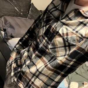 Rutig skjorta från Jack & Jones - Snygg rutig skjorta från Jack & Jones i beige, svart och blå. Skjortan har långa ärmar och knappar framtill. Perfekt för en avslappnad stil.