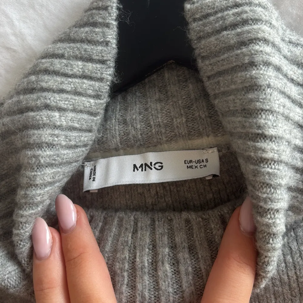Säljer en stilren grå stickad polotröja från Mango med vita detaljer längs sömmarna. Tröjan har en hög ribbad krage och långa ärmar. Passar utmärkt till både jeans och kjol. använd 1 gång!. Neuletakit & Villapaidat.