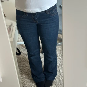 Mörkblå bootcut jeans - Snygga mörkblå bootcut jeans med klassisk femficksdesign. De har en normal passform och är perfekta för en avslappnad stil. Jeansen har dekorativa sömmar på bakfickorna som ger en extra touch.